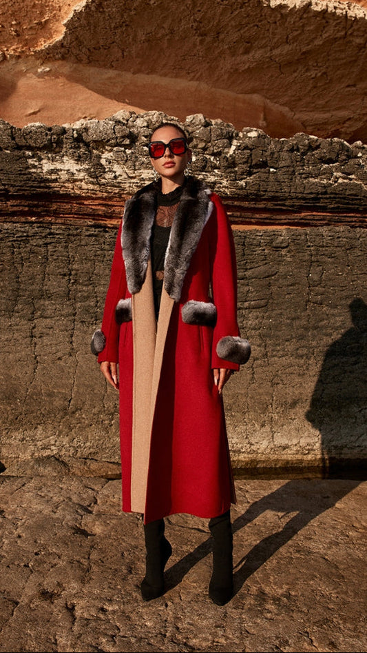 Woman wearing a red coat with fur trim standing in front of rocky terrain