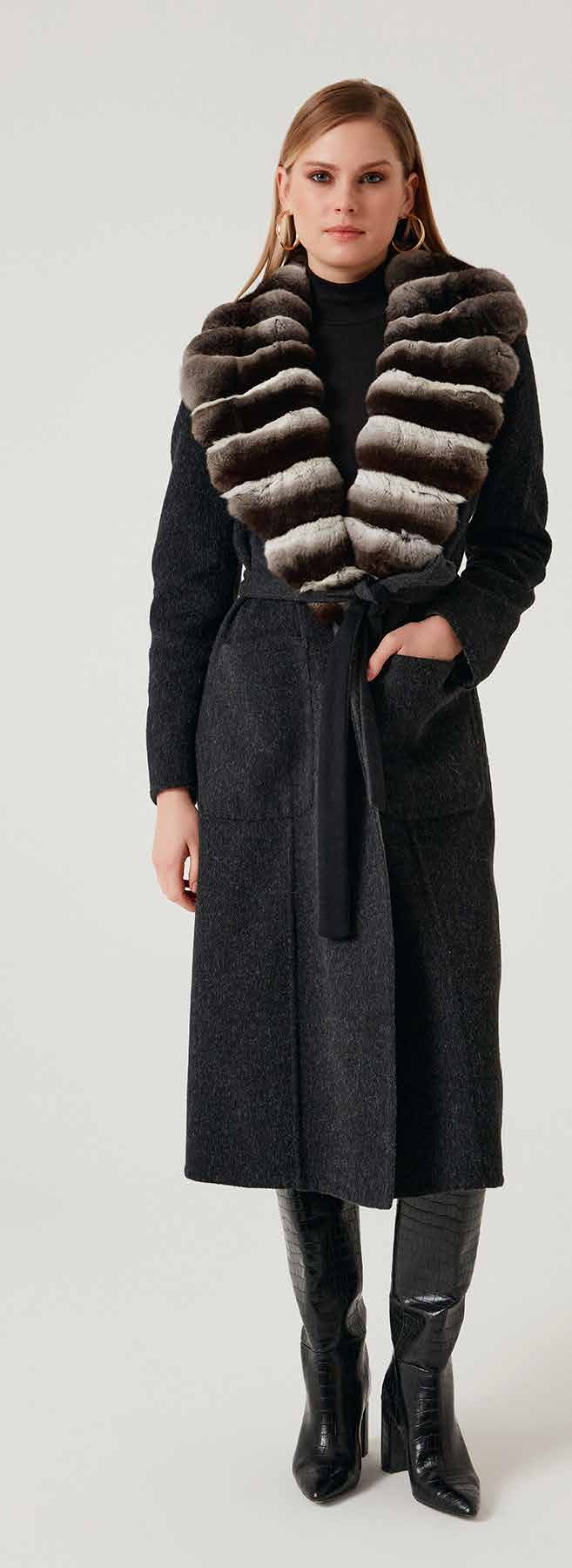 Woman wearing a long dark coat with a fur vest on a white background