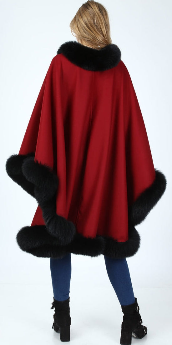 Red alpaca poncho with black fox fur trim worn by a woman on a white background