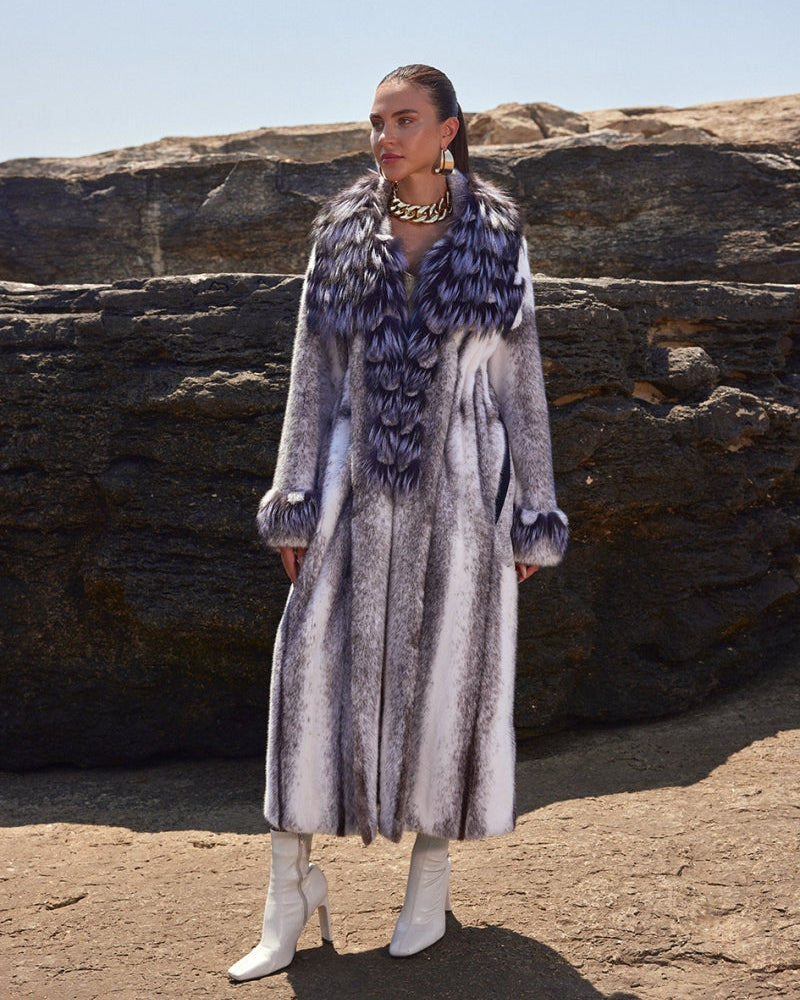 Woman wearing a long, patterned coat with fur trim standing on rocky terrain.