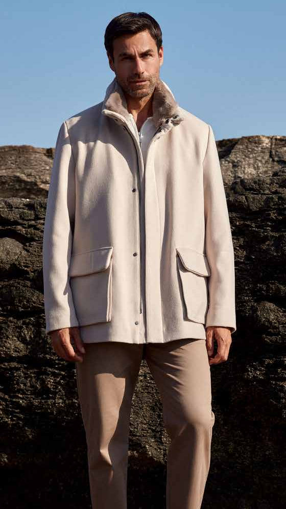 Man wearing a light-colored coat standing against a rocky background