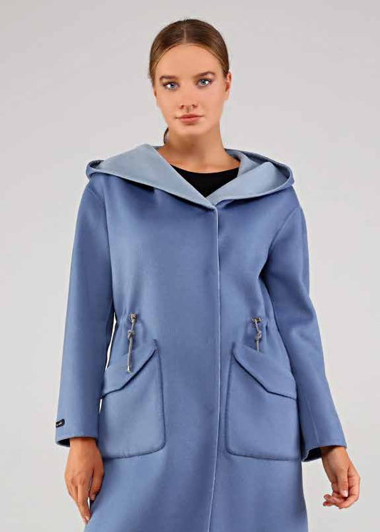 Woman wearing a long blue alpaca coat with a hood on a white background