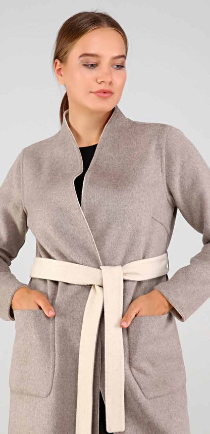 Woman wearing a gray alpaca overcoat with a belt against a plain background