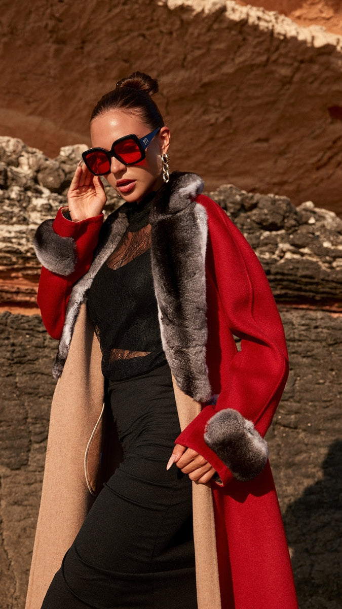 Woman wearing a red coat with fur trim and sunglasses in a desert setting