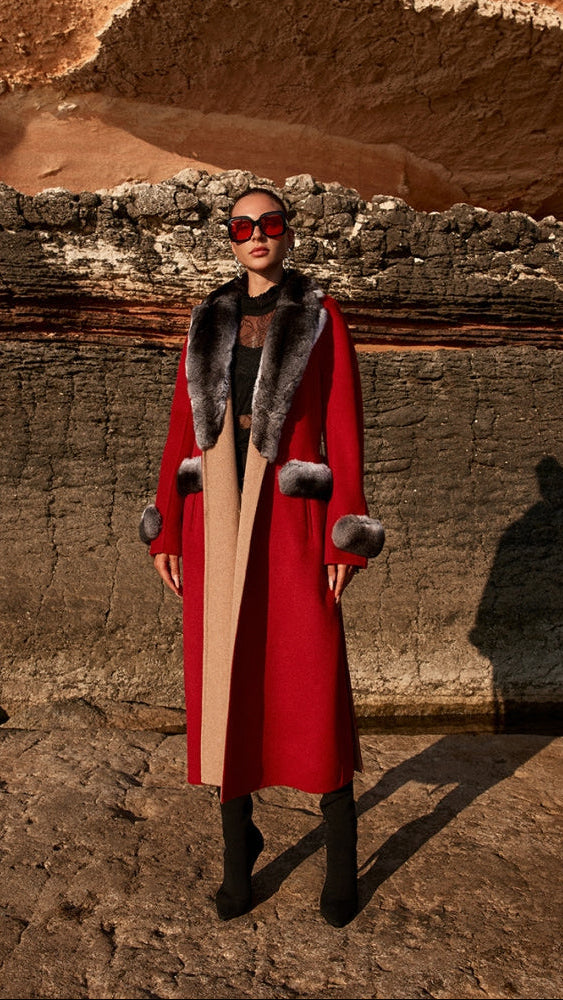 Woman wearing a red coat with fur trim standing in front of rocky terrain