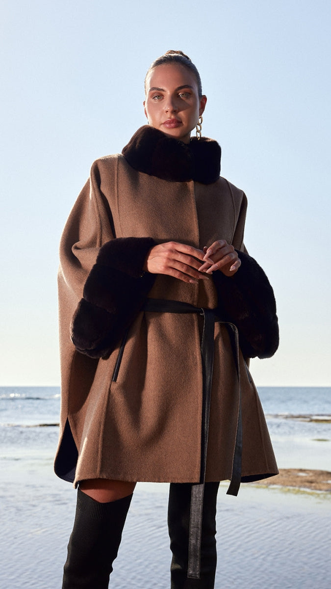 Woman wearing a brown coat with black fur trim standing on a snowy landscape.