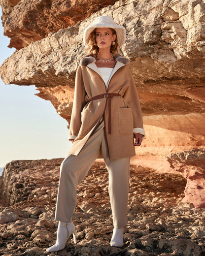 Woman in a beige coat and hat standing on rocky terrain with rock formations in the background