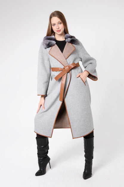 Woman wearing a long gray coat with fur trim and a brown belt on a white background