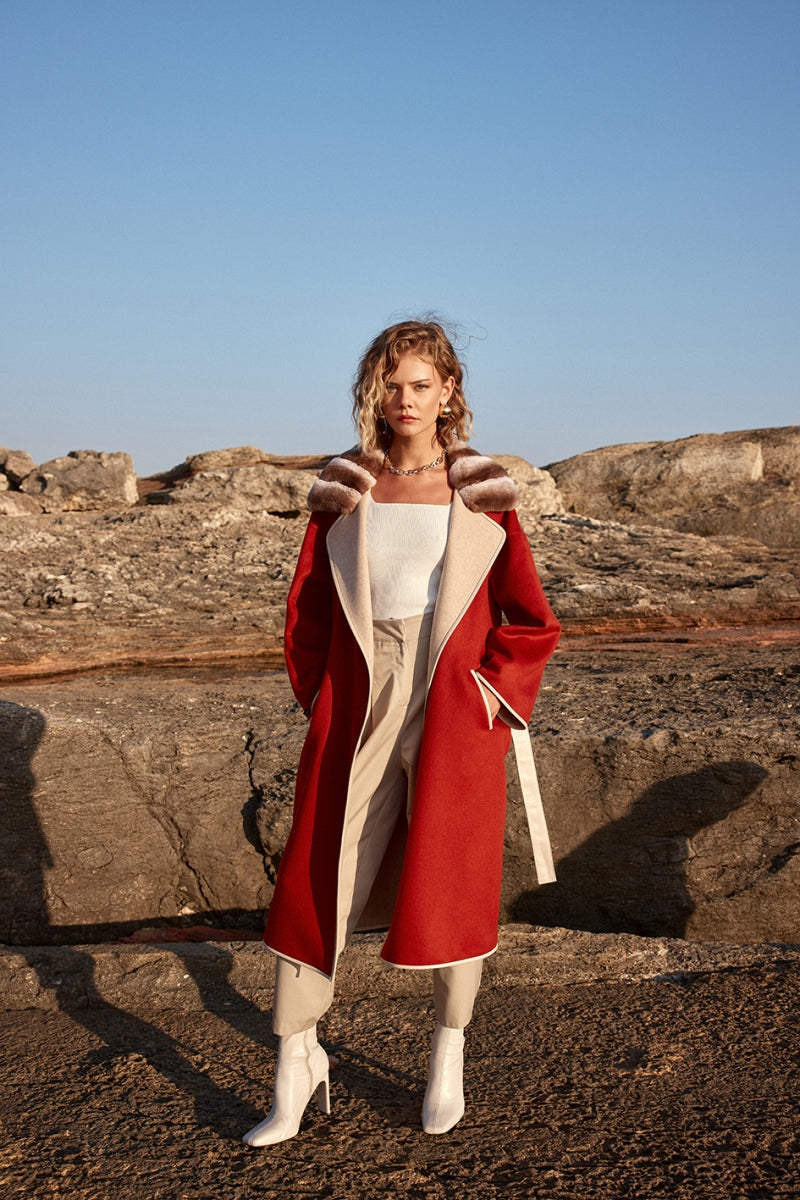 Woman in a red coat standing on rocky terrain with clear blue sky