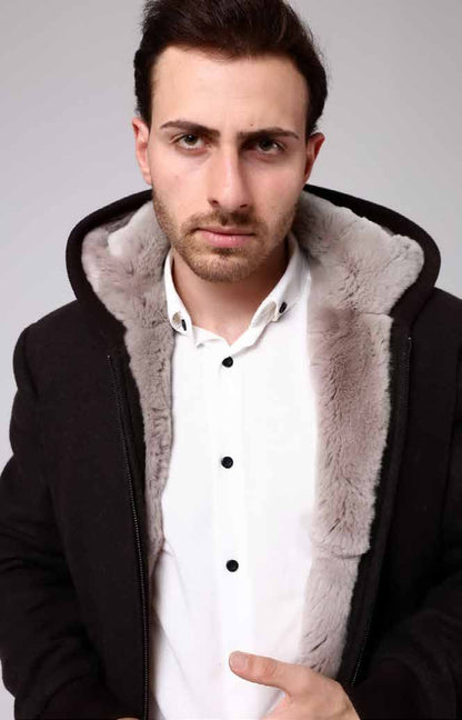 Man wearing a black coat with gray fur lining against a plain background