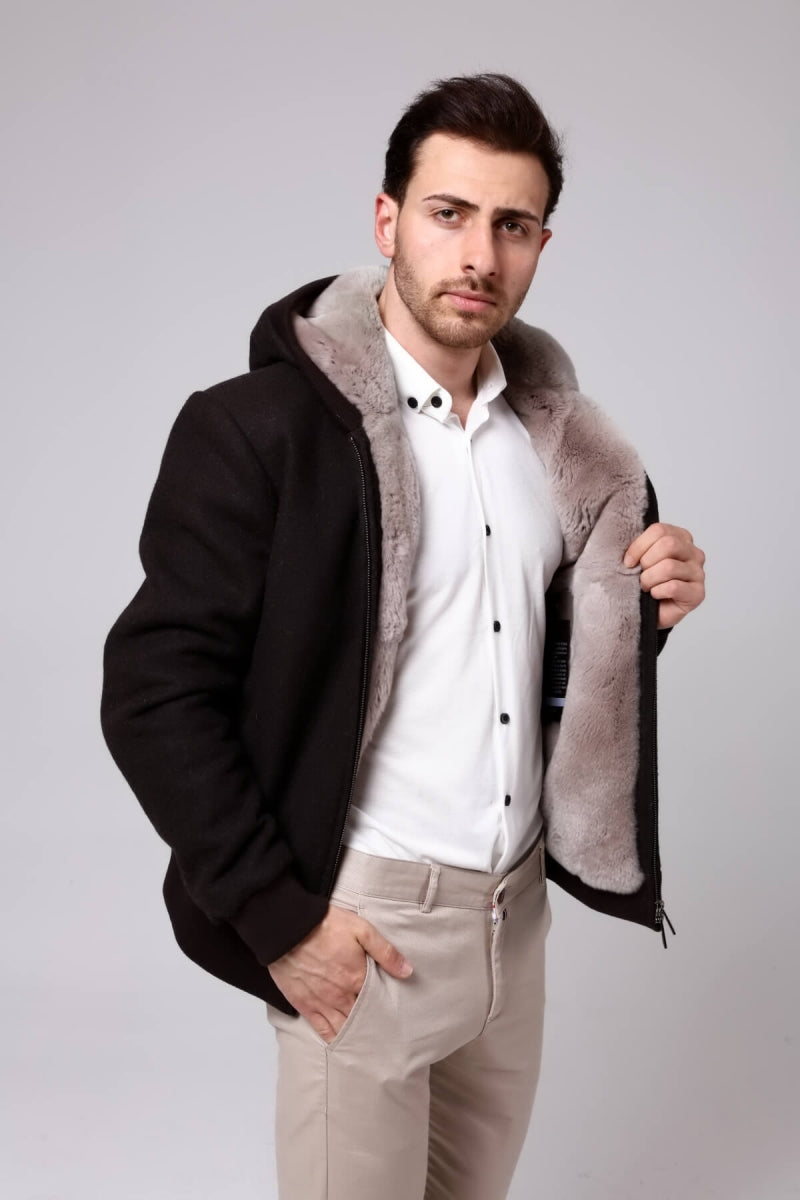 Man wearing a black coat with a fur-lined hood on a plain background