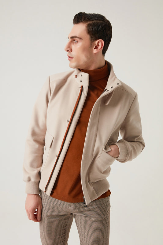 Man wearing a beige jacket over a brown shirt with a plain background