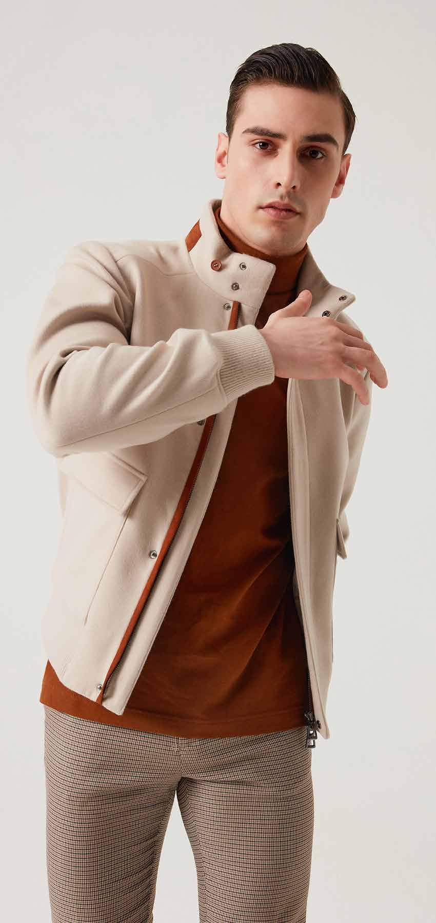 Man wearing a beige jacket over a brown shirt with a white background