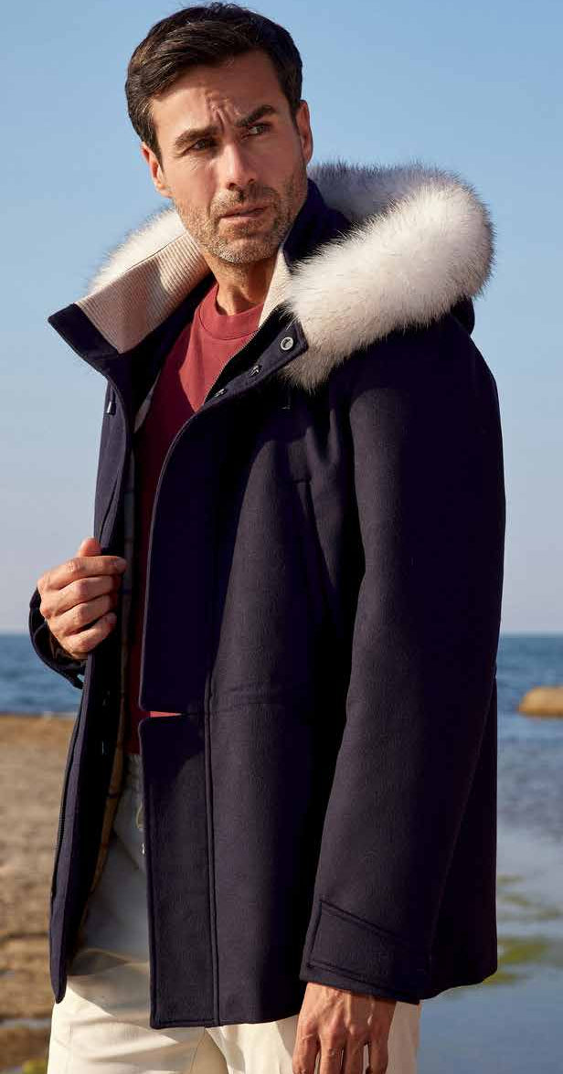 Man wearing a dark coat with a fur-lined hood by the ocean