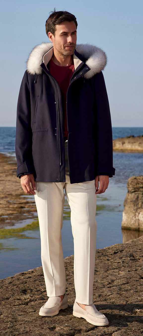 Man wearing a dark coat with a fur-lined hood by a body of water.