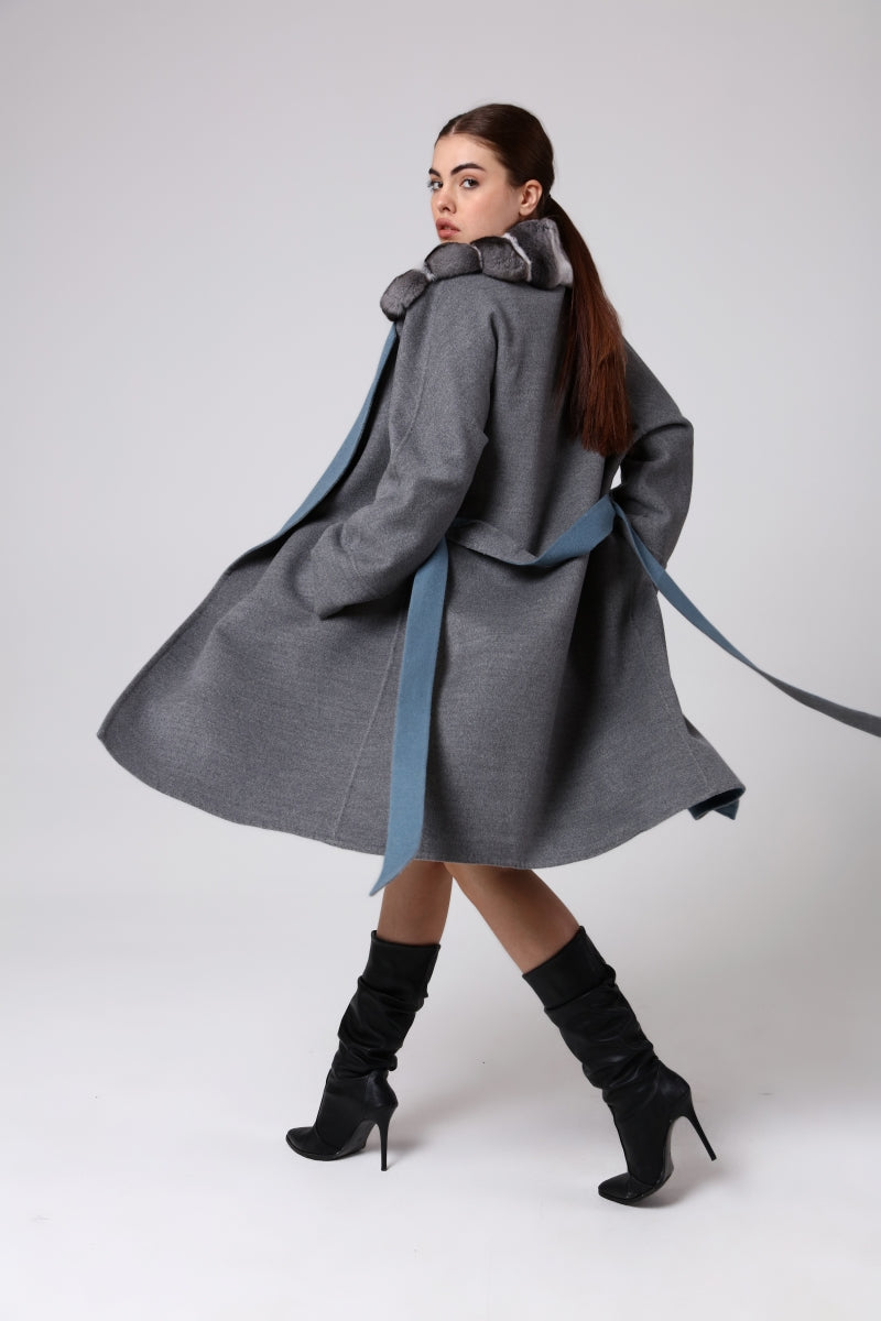 Woman wearing a long gray coat with a blue ribbon on a white background