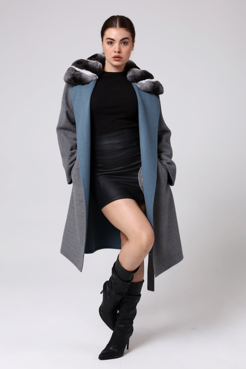 Woman wearing a long gray coat with chinchilla fur and black outfit on a white background