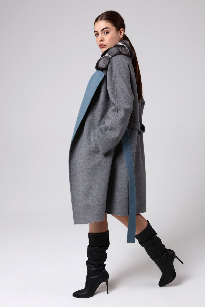 Woman wearing a long gray coat with a blue accent on a white background