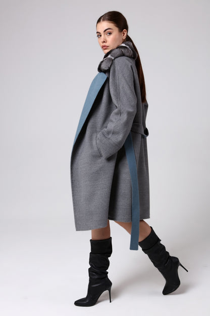 Woman wearing a long gray coat with a blue accent on a white background