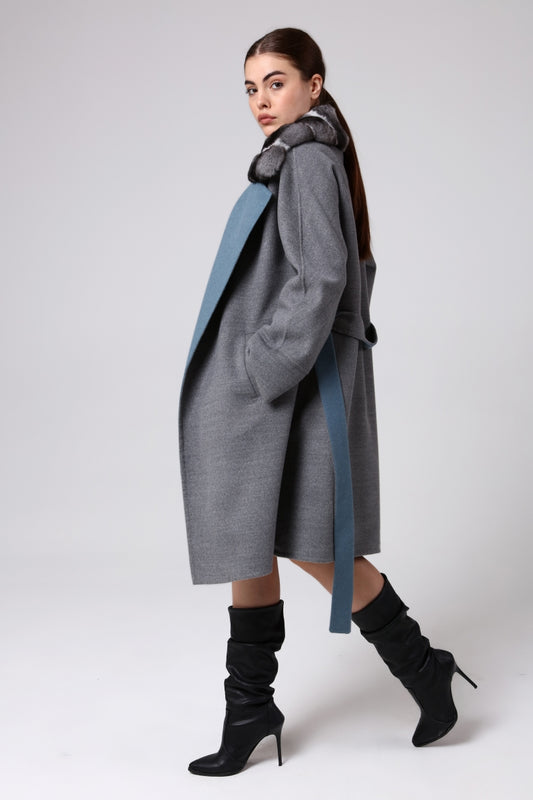 Woman wearing a long gray coat with a blue accent on a white background