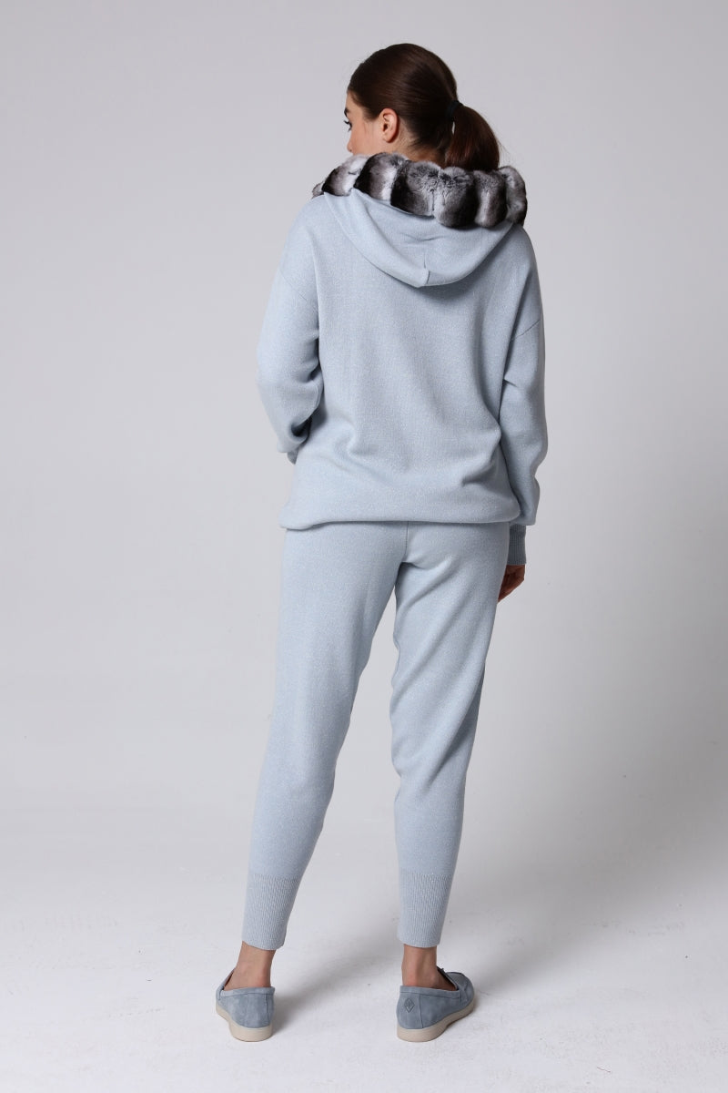 Woman wearing a light blue hoodie and pants with a chinchilla fur-lined hood on a plain background