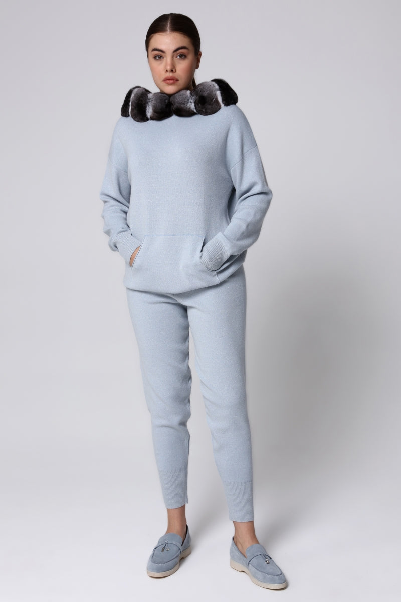 Woman wearing a light blue tracksuit with a chinchilla fur-lined hood against a white background