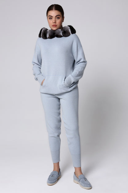 Woman wearing a light blue tracksuit with a chinchilla fur-lined hood against a white background