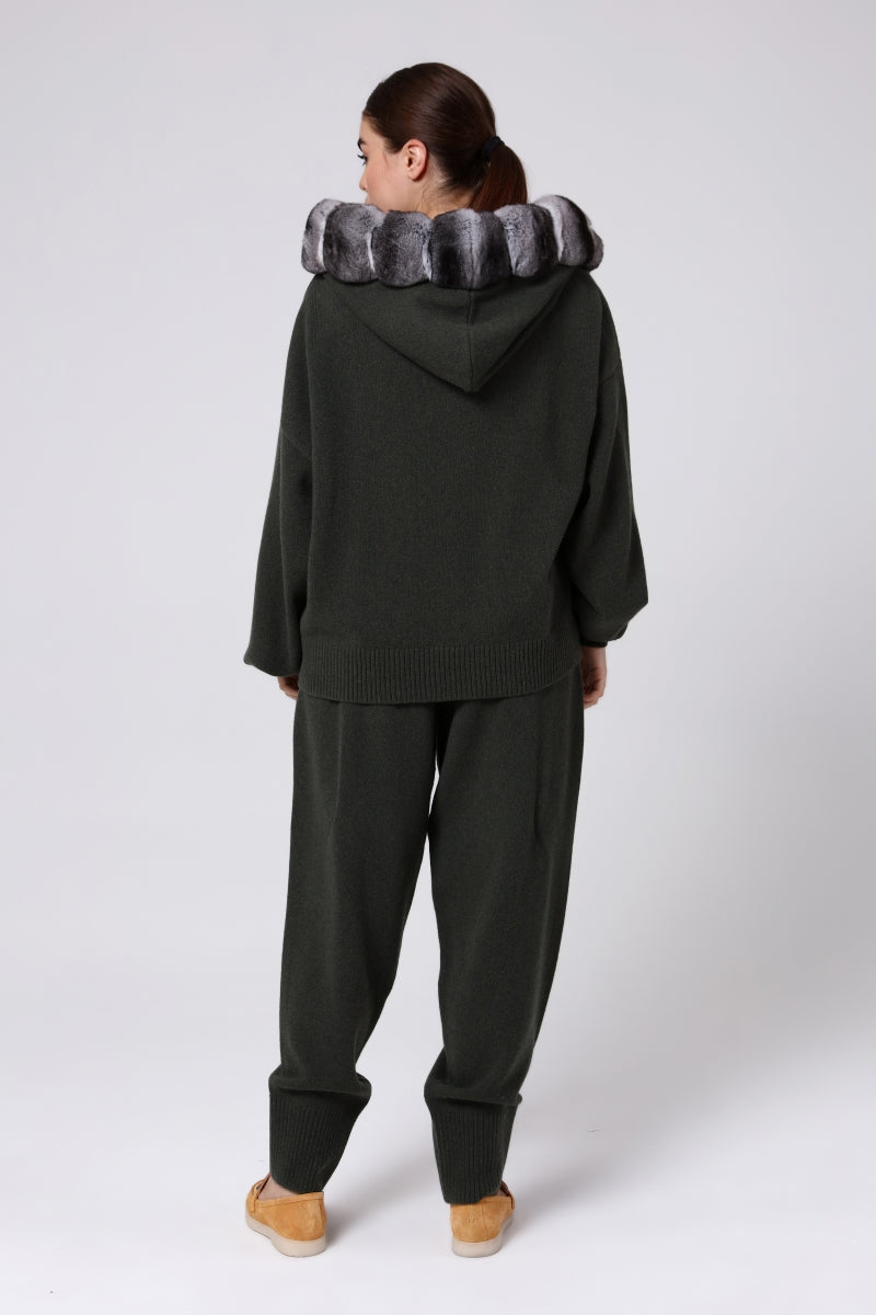 Woman wearing a dark green hoodie and pants with a chinchilla fur-lined hood on a white background