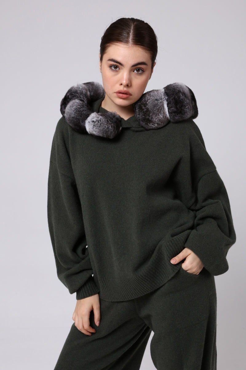 Woman wearing a dark green sweater with chinchilla fur accents on a light gray background