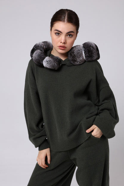 Woman wearing a dark green sweater with chinchilla fur accents on a light gray background