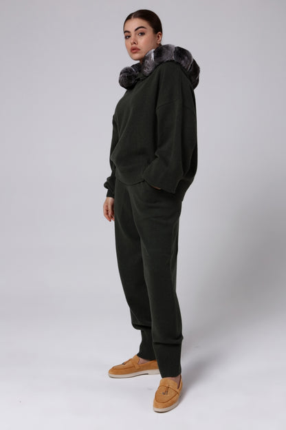 Woman wearing a dark green hoodie and pants with chinchilla fur trim on a white background