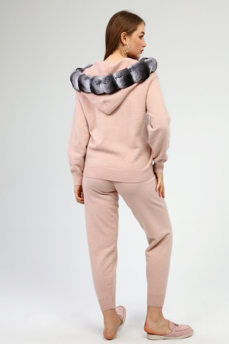 Woman wearing a pink tracksuit with a chinchilla fur-lined hood on a white background
