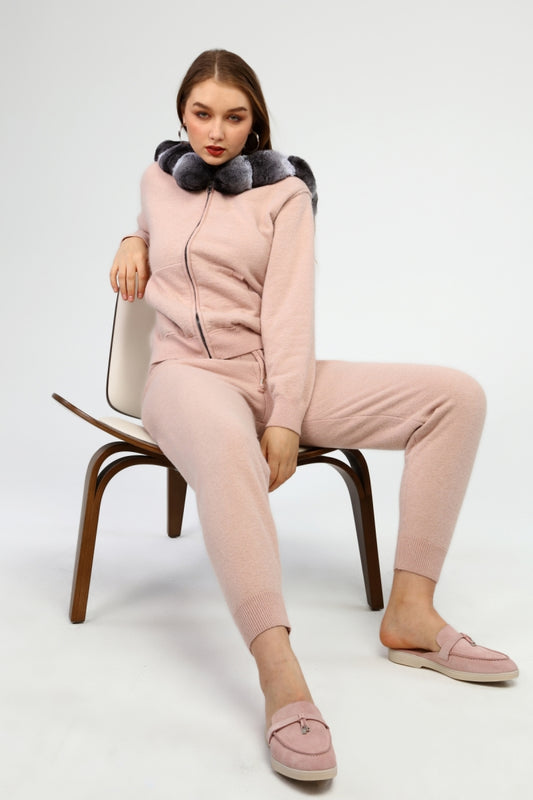 Woman sitting on a chair wearing a pink outfit with a gray chinchilla hoodie against a white background