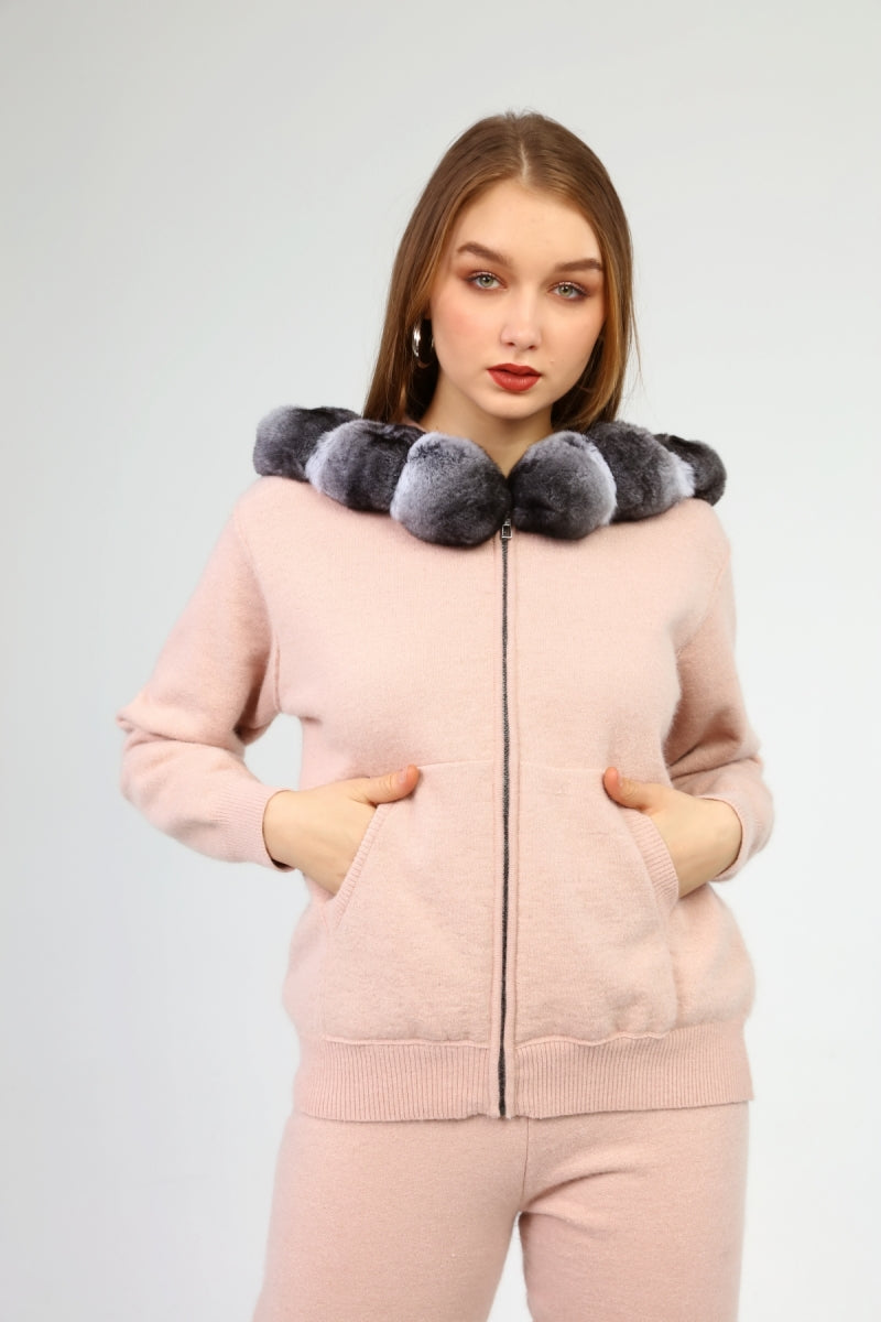 Woman wearing a pink outfit with a chinchilla fur-lined hood against a light gray background