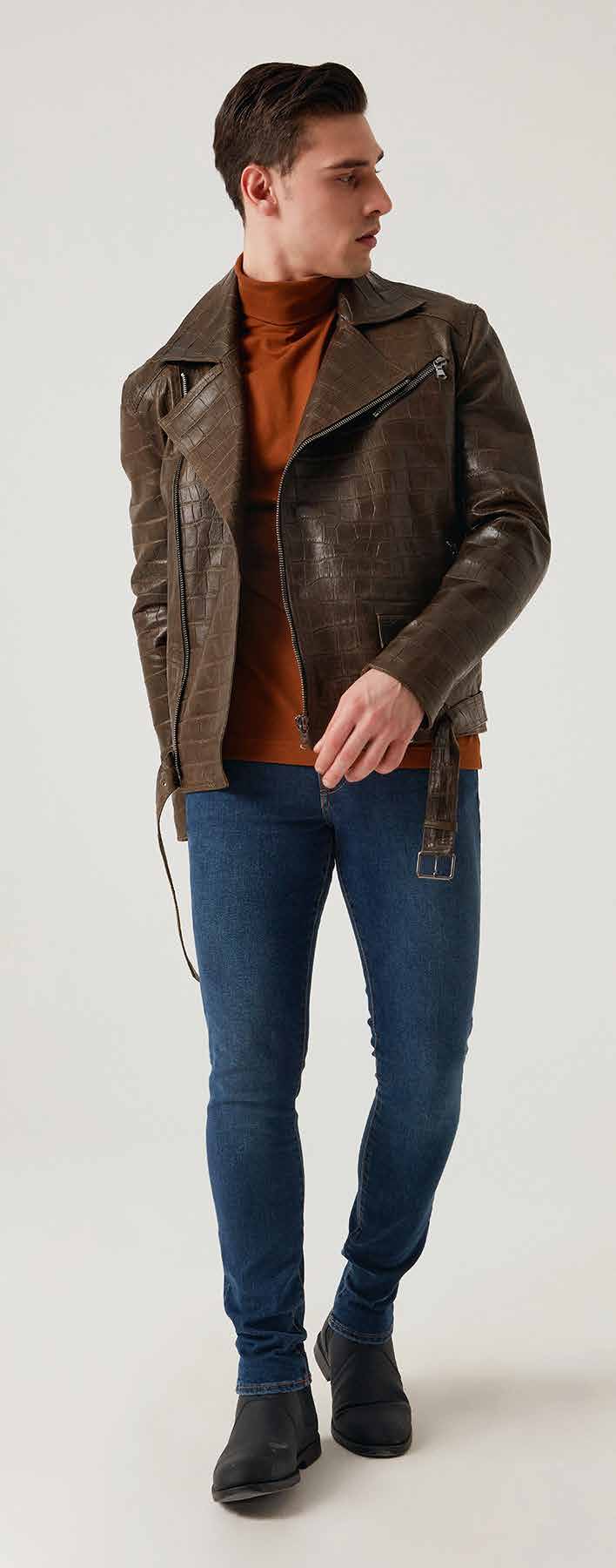 Man wearing a brown leather jacket, orange sweater, blue jeans, and black shoes on a white background