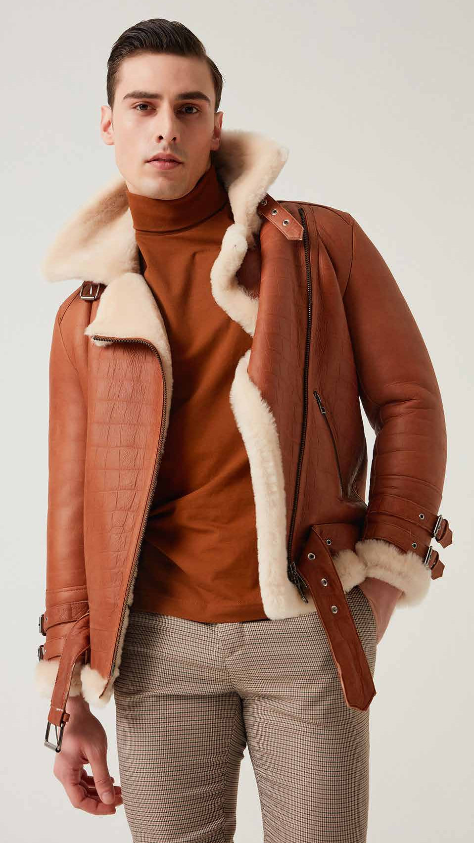 Man wearing a brown leather jacket with shearling lining on a plain background