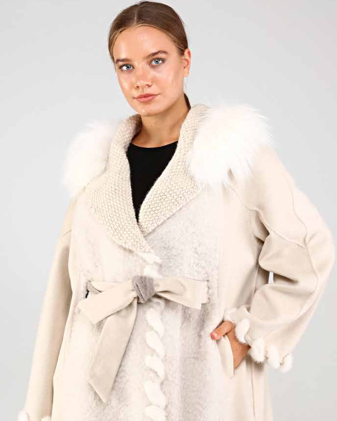 Woman wearing a cream-colored coat with mink and foxfur trim on a plain background