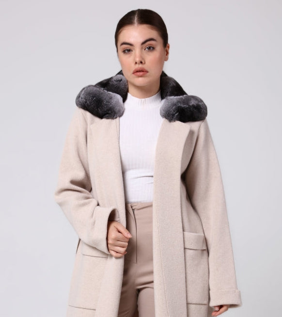 Woman wearing a long beige overcoat with chinchilla fur trim on a white background