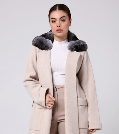 Woman wearing a long beige overcoat with chinchilla fur trim on a white background