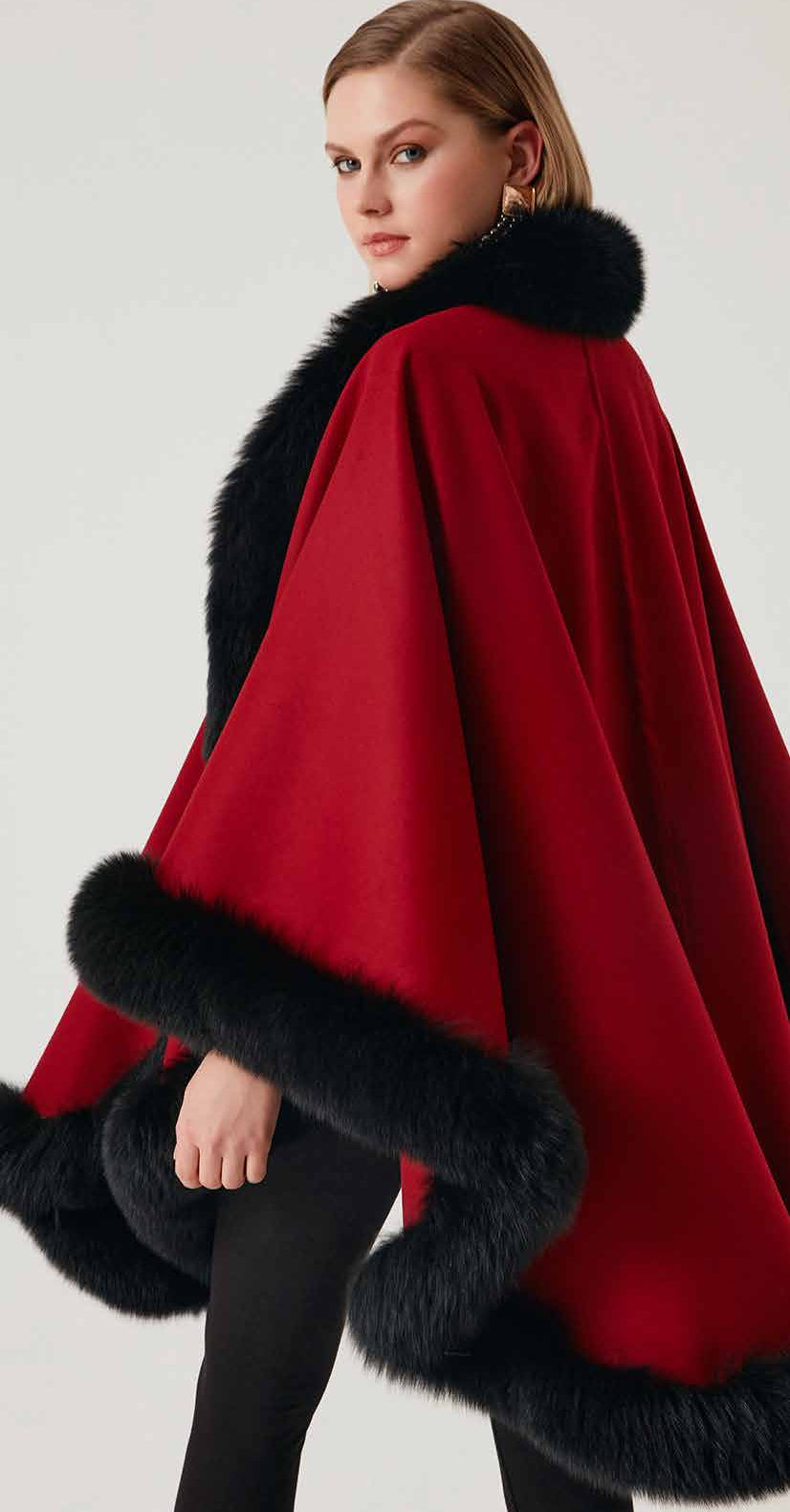 Woman wearing a red alpaca poncho with black fox fur on a white background