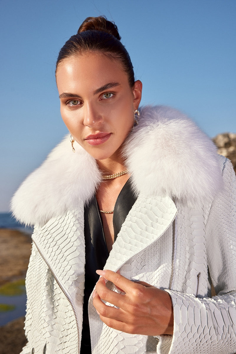 Woman wearing a white textured jacket with a fur collar outdoors on a clear day.