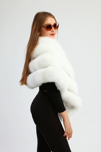 Woman wearing a white fox fur shawl over a black outfit against a plain background