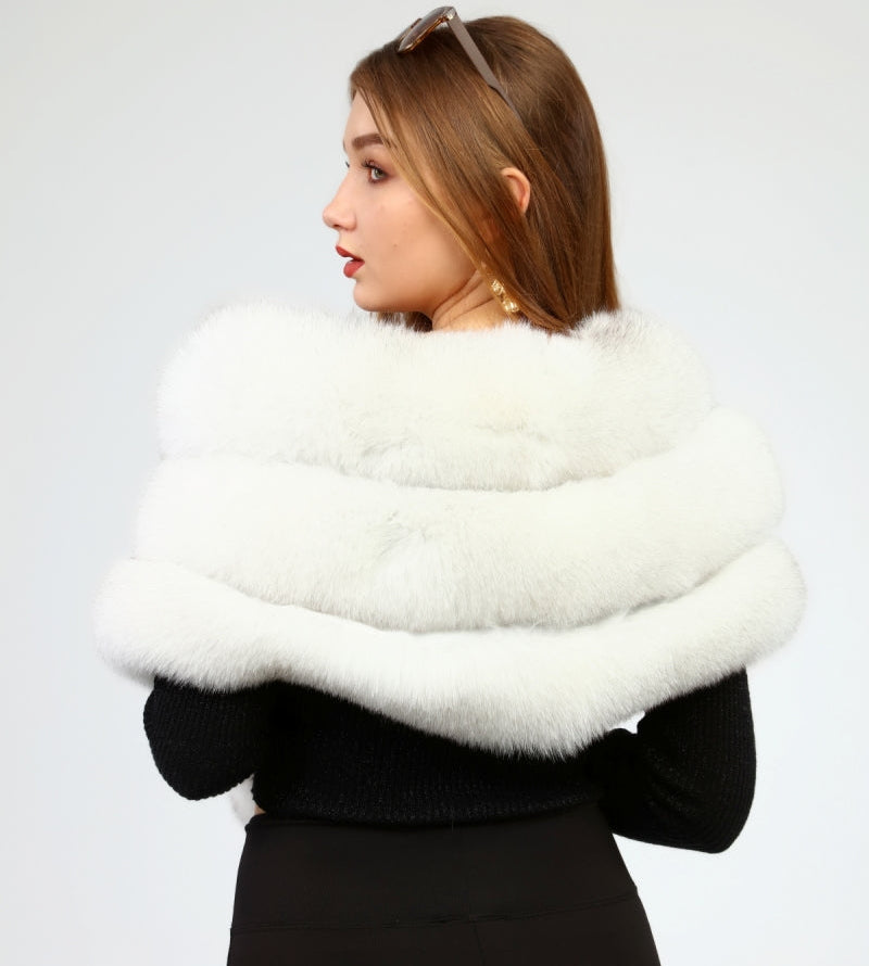 Woman wearing a white fox fur shawl over a black outfit on a light gray background