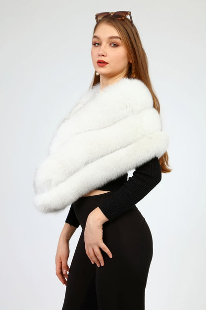 Woman wearing a white fox fur shawl over a black outfit on a plain background