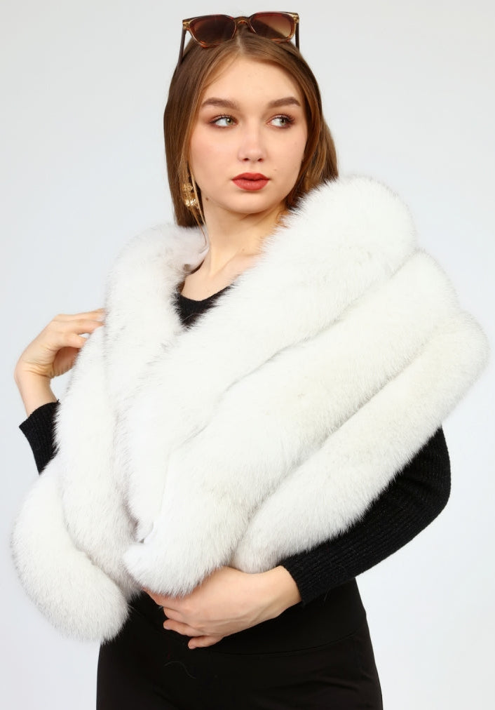 Woman wearing a white fox fur shawl over a black outfit against a plain background