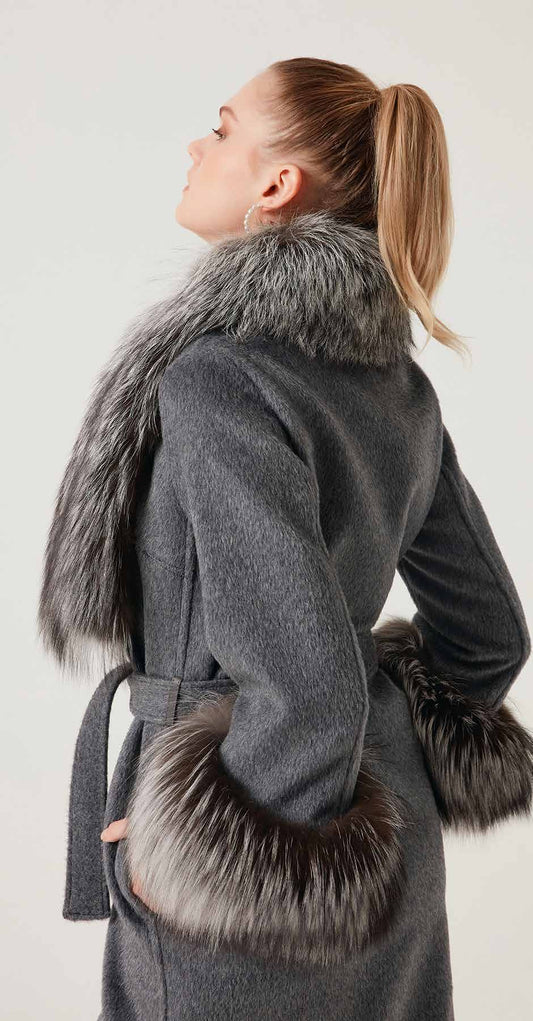 Woman wearing a gray coat with fur accents on a plain background
