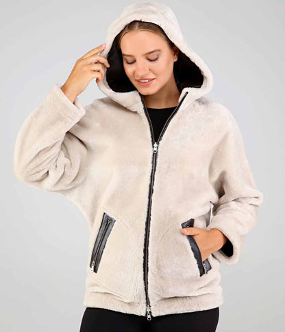 Woman wearing a beige fleece jacket with a hood on a gray background