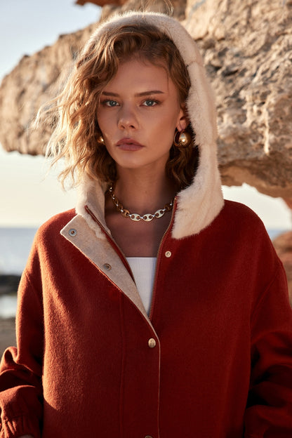 Woman wearing a red coat with a fur-lined hood in a natural setting