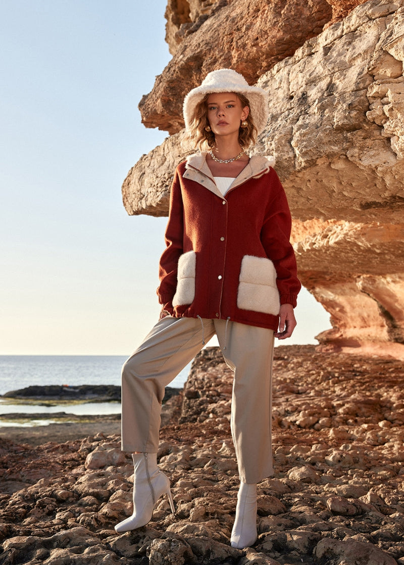 Woman in a red jacket and beige hat standing on rocky terrain with ocean view