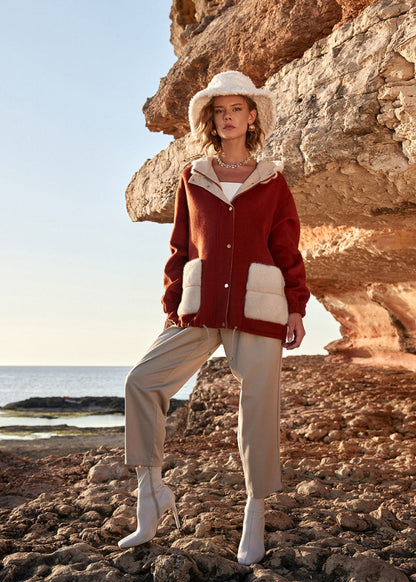 Woman in a red jacket and beige hat standing on rocky terrain with ocean view